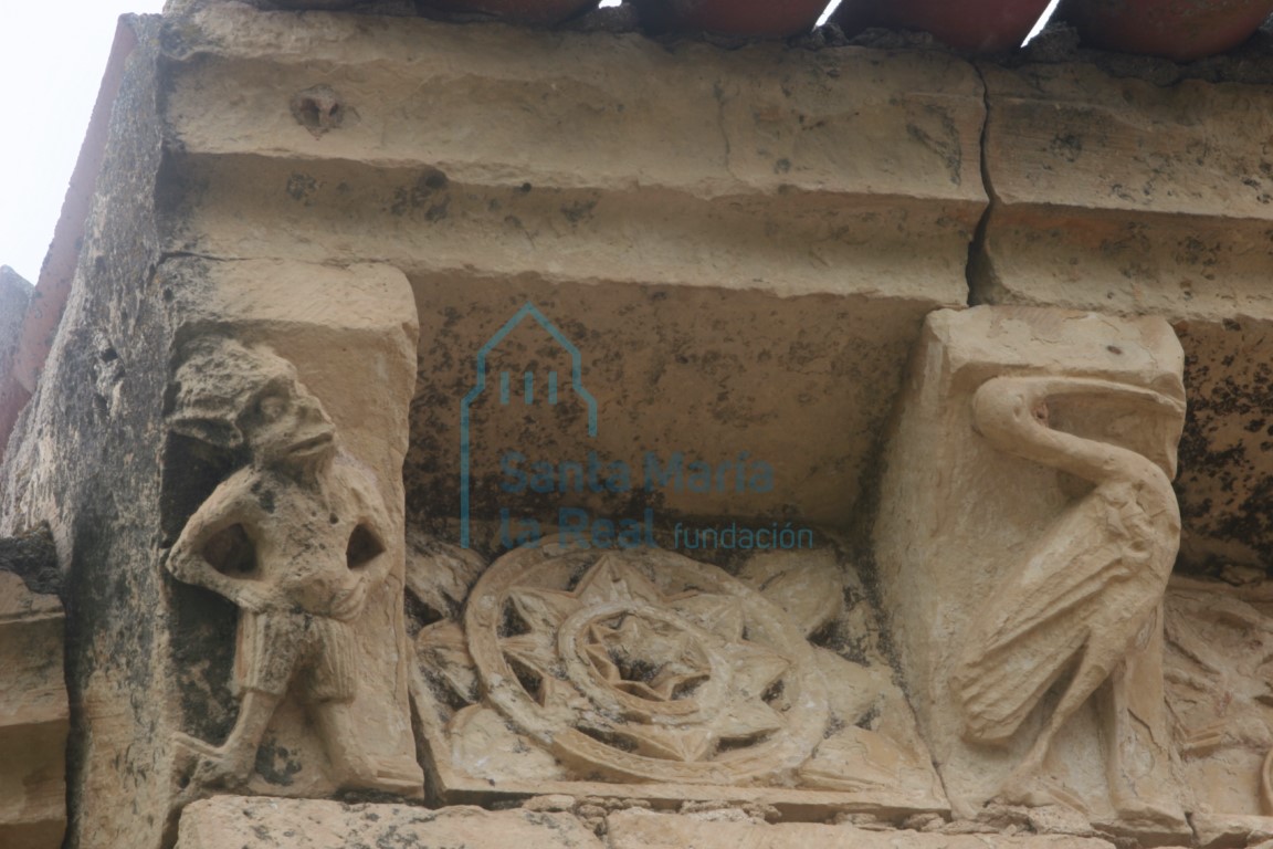 Canecillos de un diablo y una cigüeña y metopa decorada con roseta, en el muro norte del presbiterio