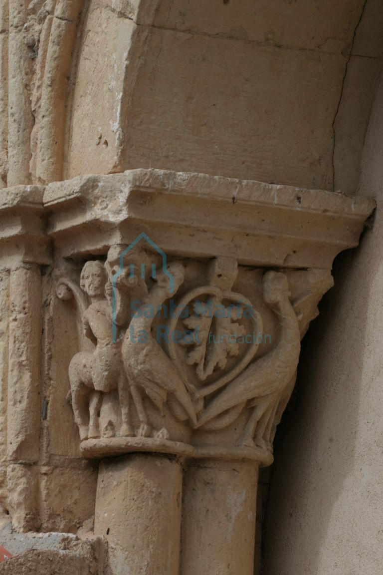 Capitel de la galería porticada figurada con ornamento en los ángulos de sendos centauros-sagitario de cabellera rematada en brotes vegetales que tensan sus arcos hacia estilizadas arpías de largo cuello vuelto