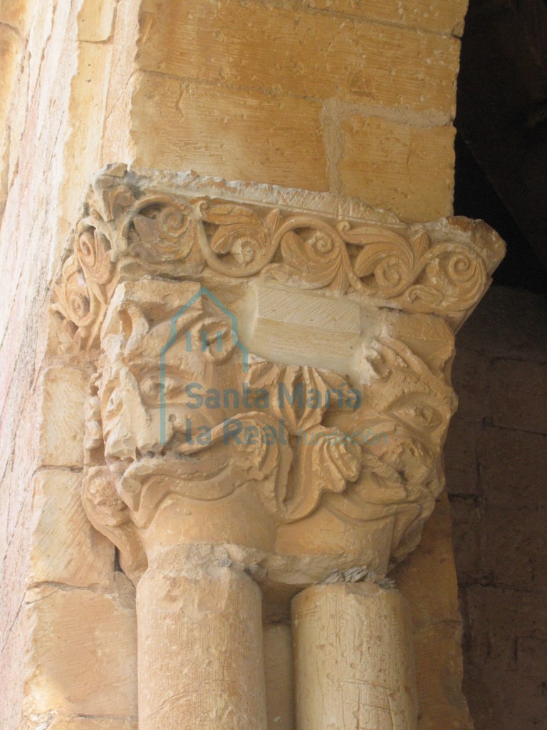 Capitel con dos mascarones que asemejan un felino mostrando las fauces, en el lado meridional del pórtico
