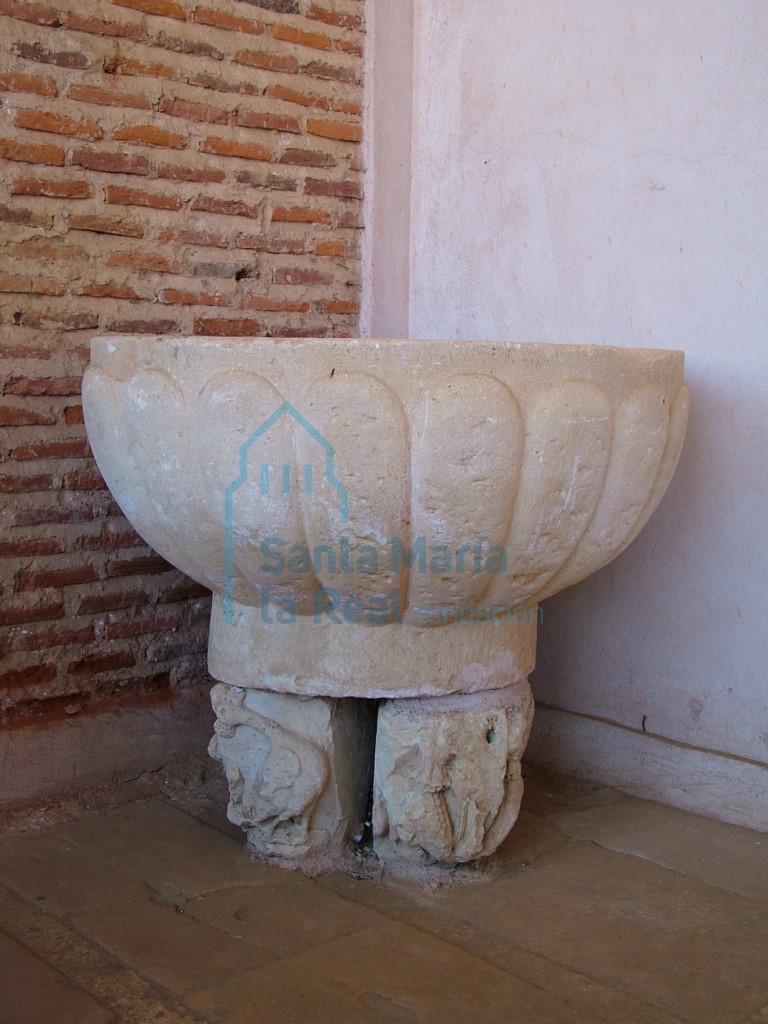 Pila bautismal con el vaso decorado con gallones. Como pie se han utilizado dos capiteles, bastante deteriorados, ambos decorados con aves en sólo dos de sus frentes