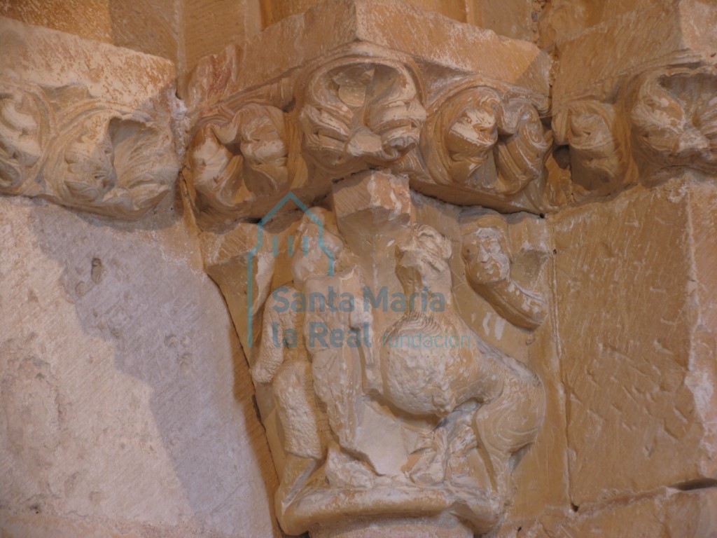 Capitel interior del lado derecho ornado con un guerrero enfrentandose a un grifo, mientras la escena es observada por una cabeza que se asoma tras el grifo